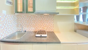 A kitchen with a tiled backsplash, a sink, a stove, and cabinets. - Cozy And Spacious Studio Apartment At Taman Melati Jatinangor (Hegarmanah)