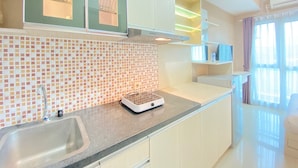 A modern kitchen with a tiled backsplash, a stainless steel sink, and a built-in oven. - Cozy And Spacious Studio Apartment At Taman Melati Jatinangor (Hegarmanah)