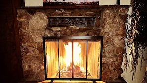 A stone fireplace with a fire, a patterned rug, and a wall-mounted artwork above it. - Ultimate relaxation on 4+ acres, hot tub, projector/game room, BBQ, stars, moon (Yucca Valley)