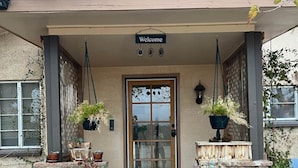 A building with a 'Welcome' sign above the entrance, stone steps leading up to a wooden door, and potted plants on either side. - Ultimate relaxation on 4+ acres, hot tub, projector/game room, BBQ, stars, moon (Yucca Valley)