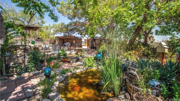 A garden with a pond, stone pathway, wooden pergola, and outdoor seating area. - Ultimate relaxation on 4+ acres, hot tub, projector/game room, BBQ, stars, moon (Yucca Valley)