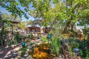 A garden with a pond, stone pathway, wooden pergola, and outdoor seating area. - Ultimate relaxation on 4+ acres, hot tub, projector/game room, BBQ, stars, moon (Yucca Valley)