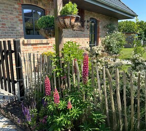 Une maison en briques avec une clôture en bois, un pot suspendu contenant des plantes vertes et une variété de plantes à fleurs dans le jardin.