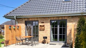 A house with a tiled roof, a brick exterior, a patio with outdoor furniture, and a lawn.