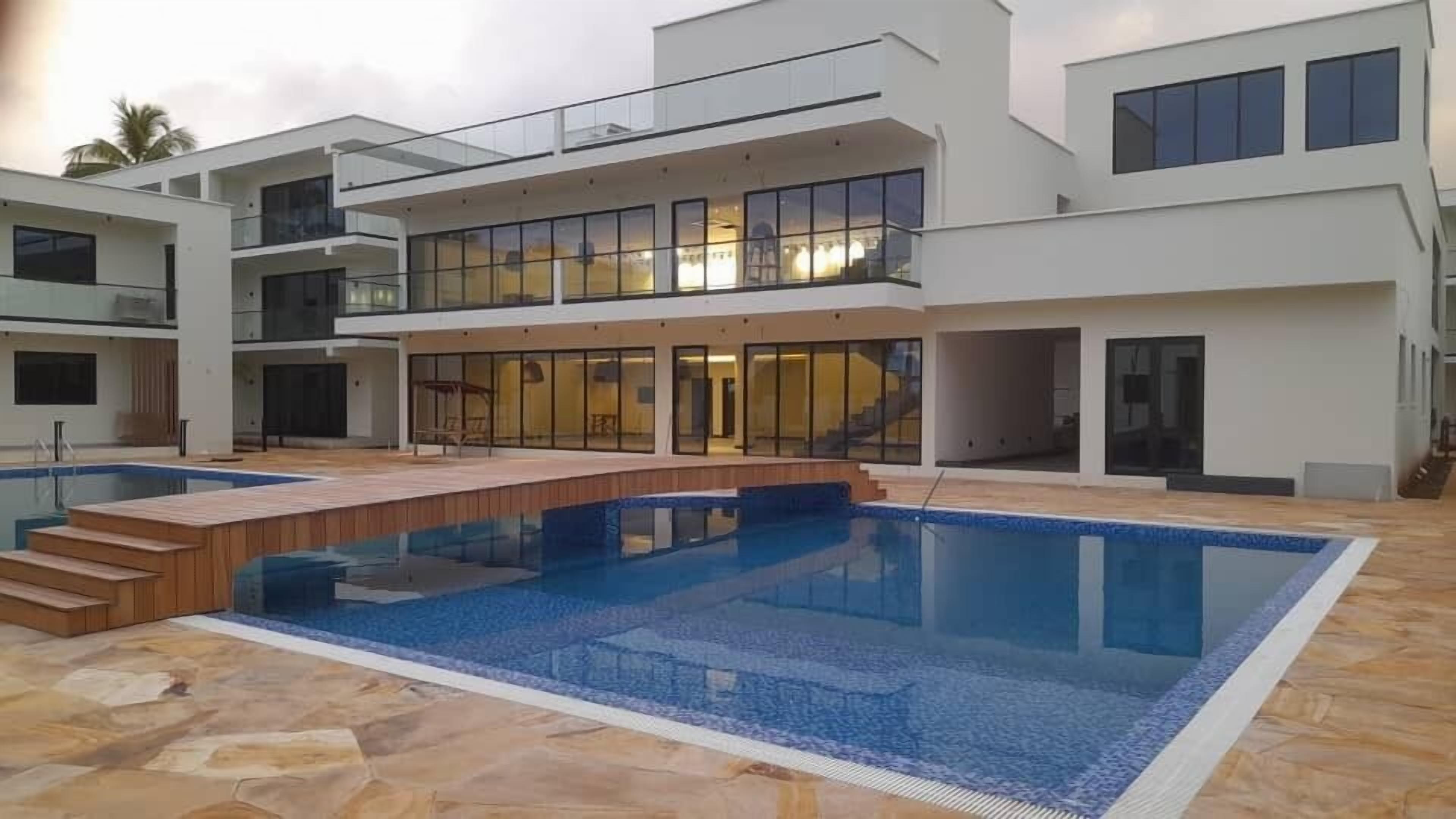 Une maison moderne à plusieurs étages, dotée d’un espace piscine central, de grandes baies vitrées et d’une terrasse en bois.