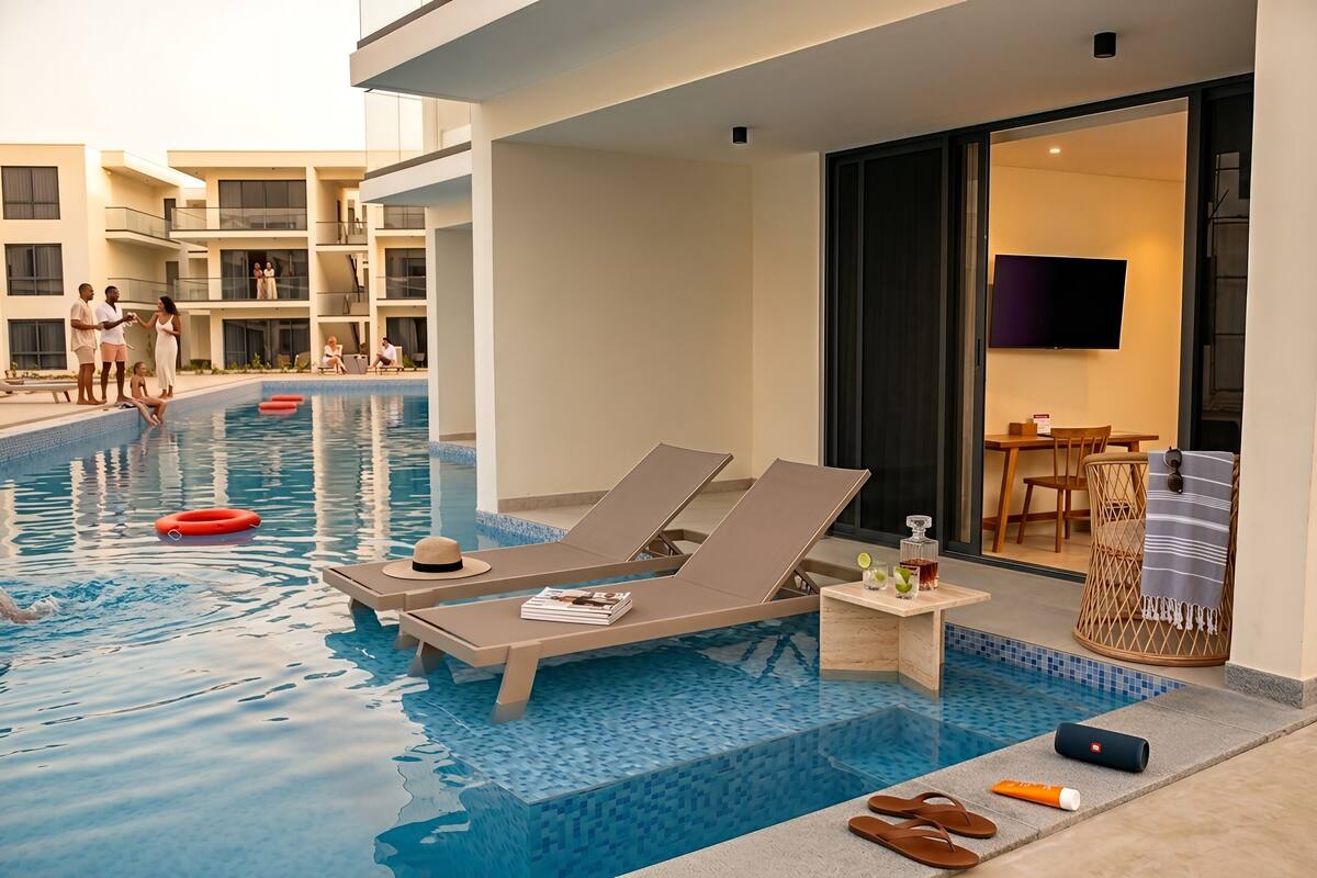 A swimming pool with lounge chairs, a small table with drinks, and a TV mounted on the wall.