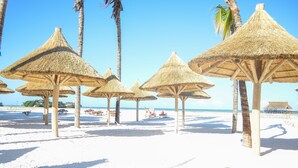A beach with thatched umbrellas and palm trees. - TOA Hotel & Spa Zanzibar (Pongwe)