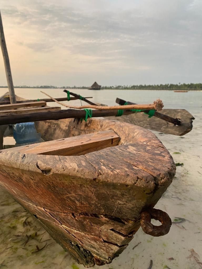 A wooden boat with a curved bow resting on a sandy shore.