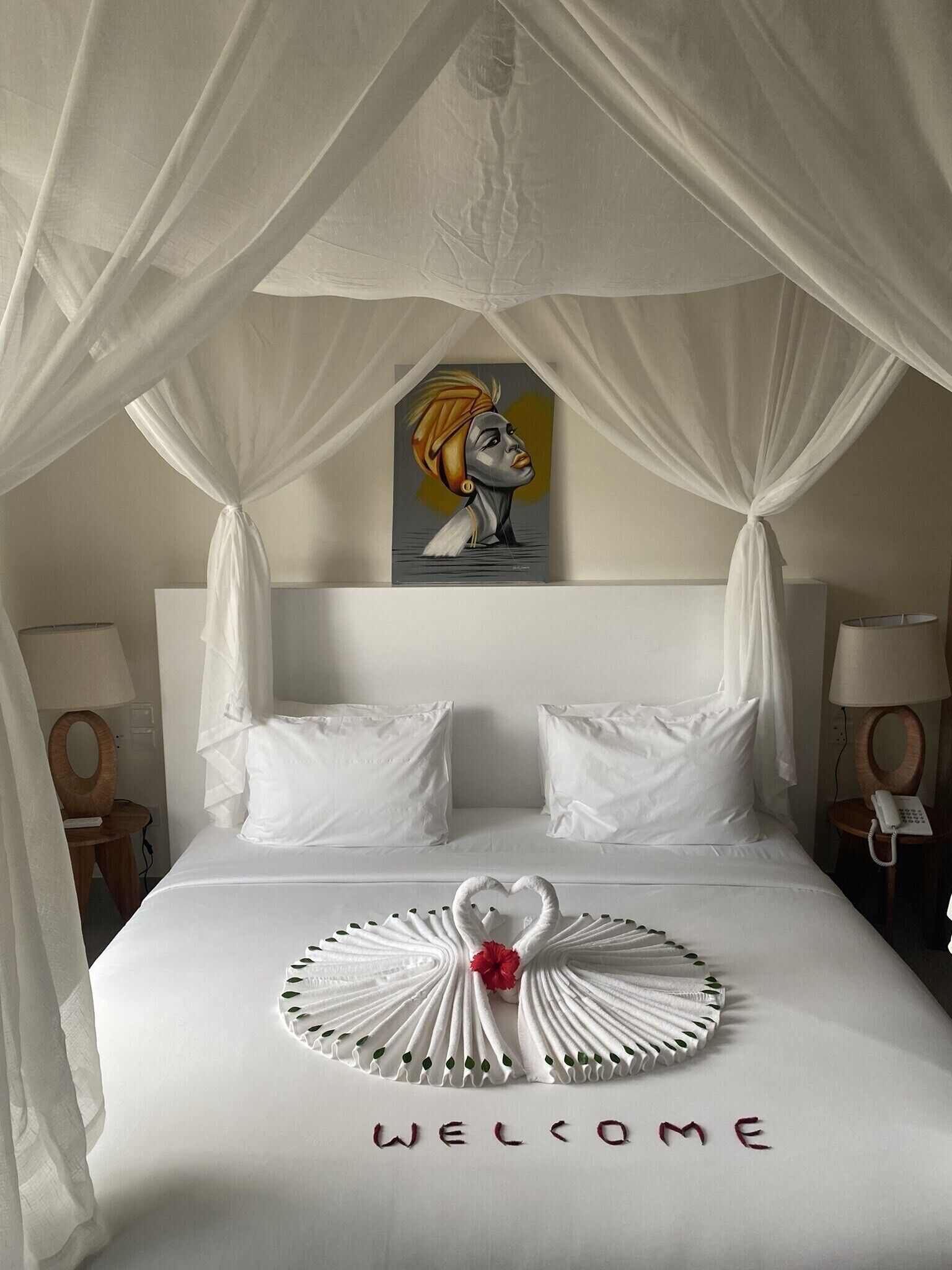 Una camera d'albergo con un letto a baldacchino, biancheria da letto bianca, un tappetino di benvenuto e un quadro appeso al muro.