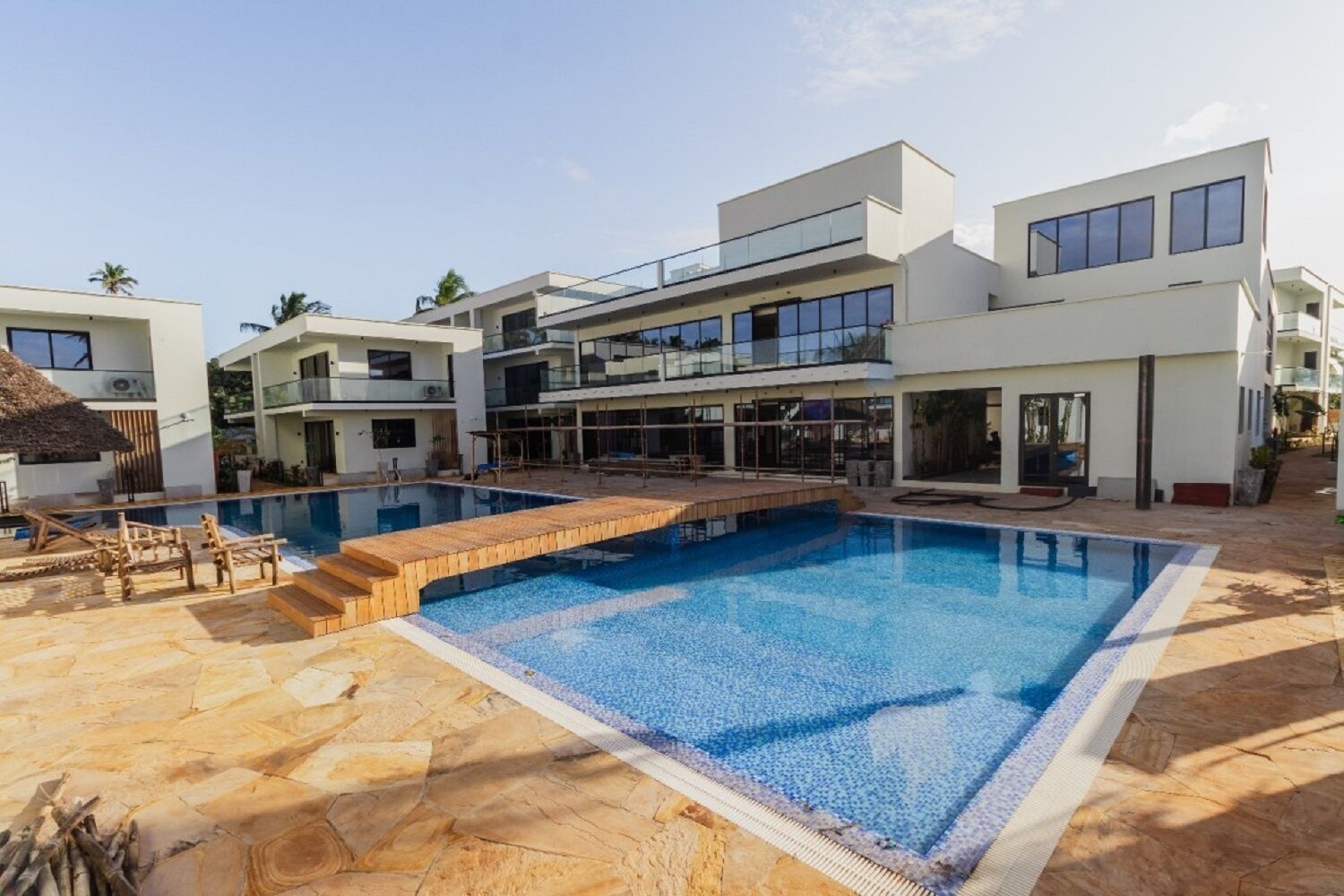 A modern multi-story building with a large central pool, outdoor seating, and a clear sky.