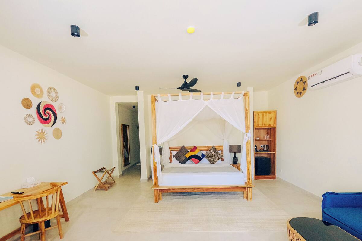 A room with a bed, a desk, a chair, a blue sofa, and a wall with decorative items.