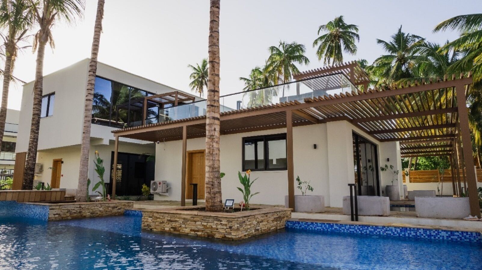 Un resort moderno con piscina, palmeras y un espacio al aire libre techado.