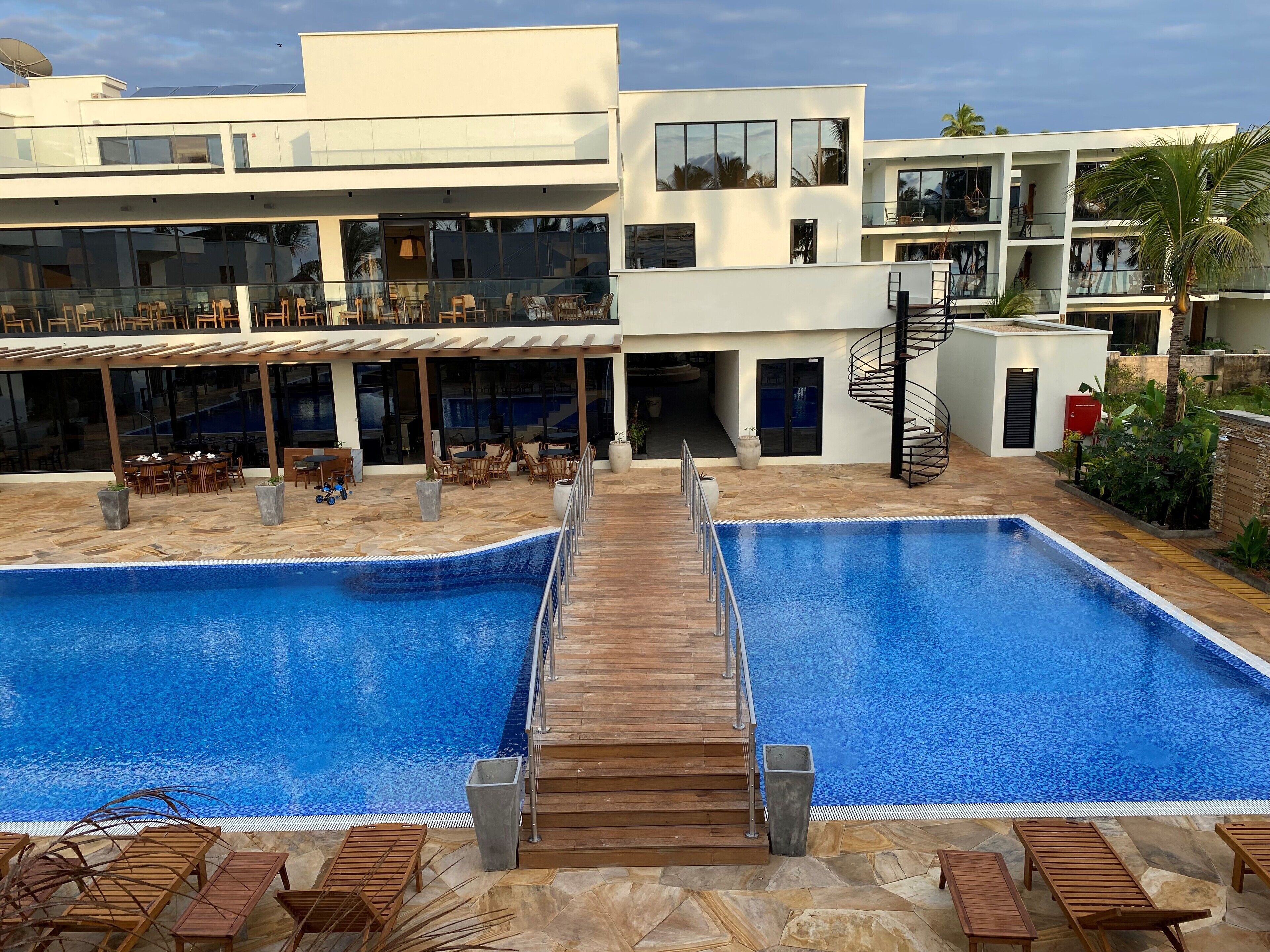 A modern hotel with two swimming pools, outdoor seating, and a covered area with tables and chairs.