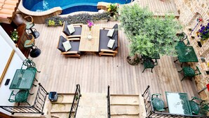 Uma área de piscina no terraço com deck de madeira, piscina, móveis de exterior e plantas em vasos.