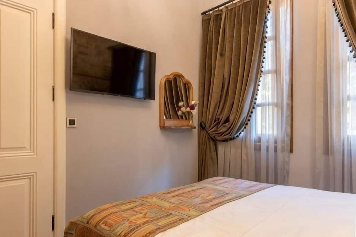 Una camera da letto con un letto, una televisione a muro e una finestra con tende.