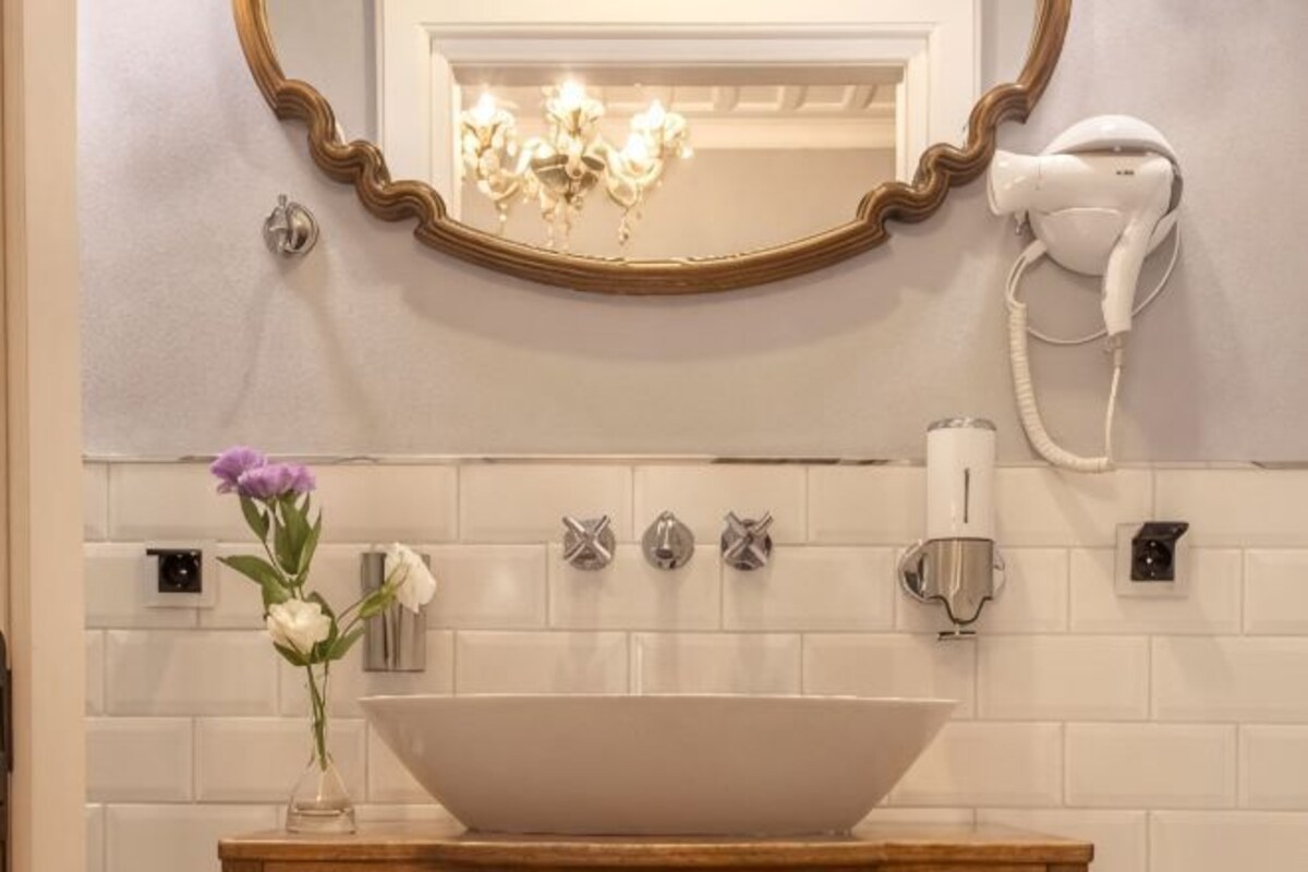 Un bany amb un lavabo blanc, un mirall amb marc daurat, un assecador d'eixugat i un ram de flors.