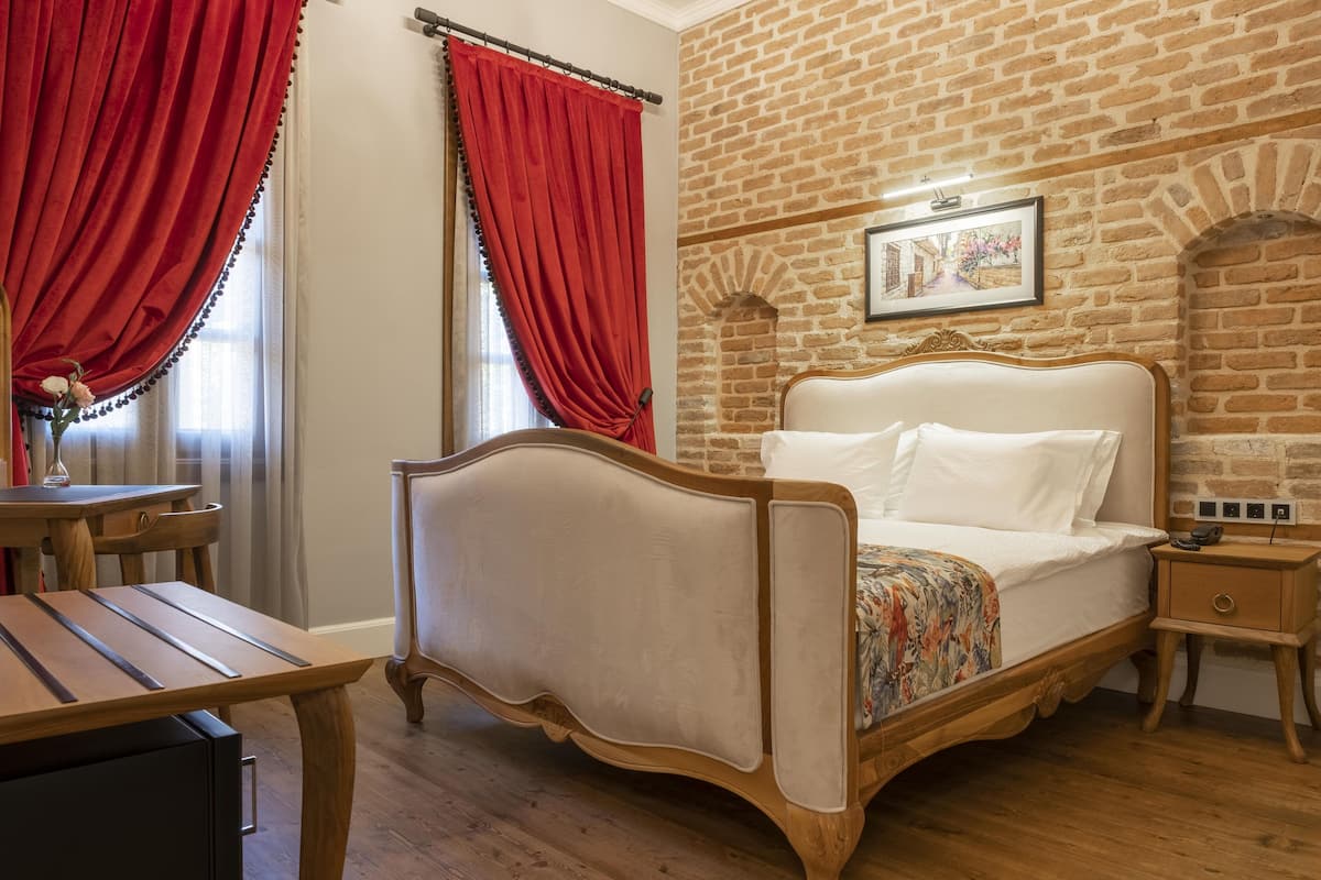 Una camera da letto con un letto di legno, tende rosse, un muro in mattoni e un tavolino con un vaso.