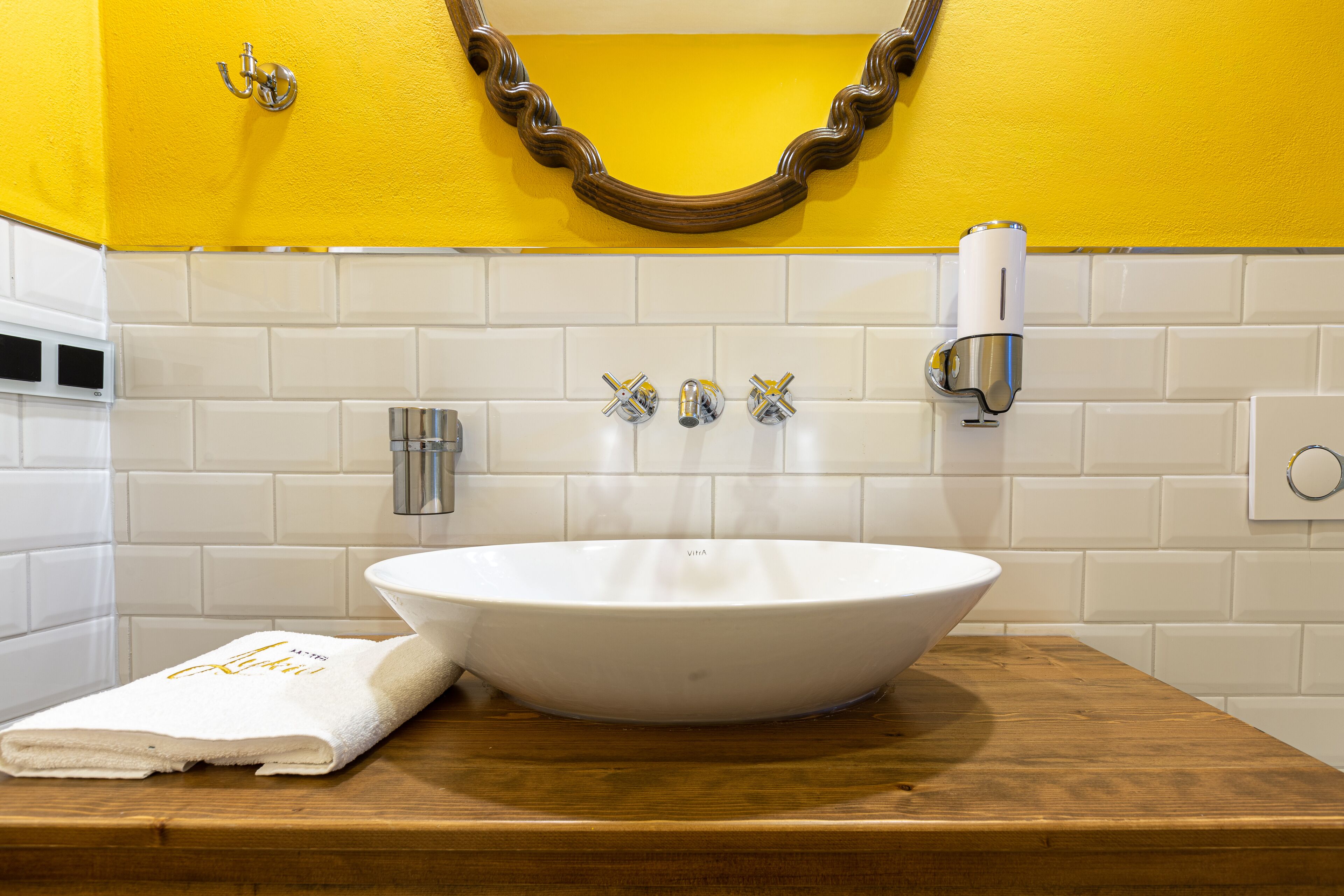 Un bagno con un lavandino bianco, tre rubinetti, un asciugamano e uno specchio con cornice in legno.