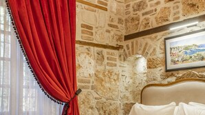 Quarto com parede de pedra, cama com roupa de cama branca, cortina vermelha e um candelabro.