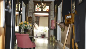 Um corredor com uma cadeira vermelha, um cavalete de madeira e um vaso com flores.