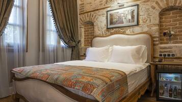 A bedroom with a wooden bed, a patterned bedspread, a brick wall, and a small refrigerator.