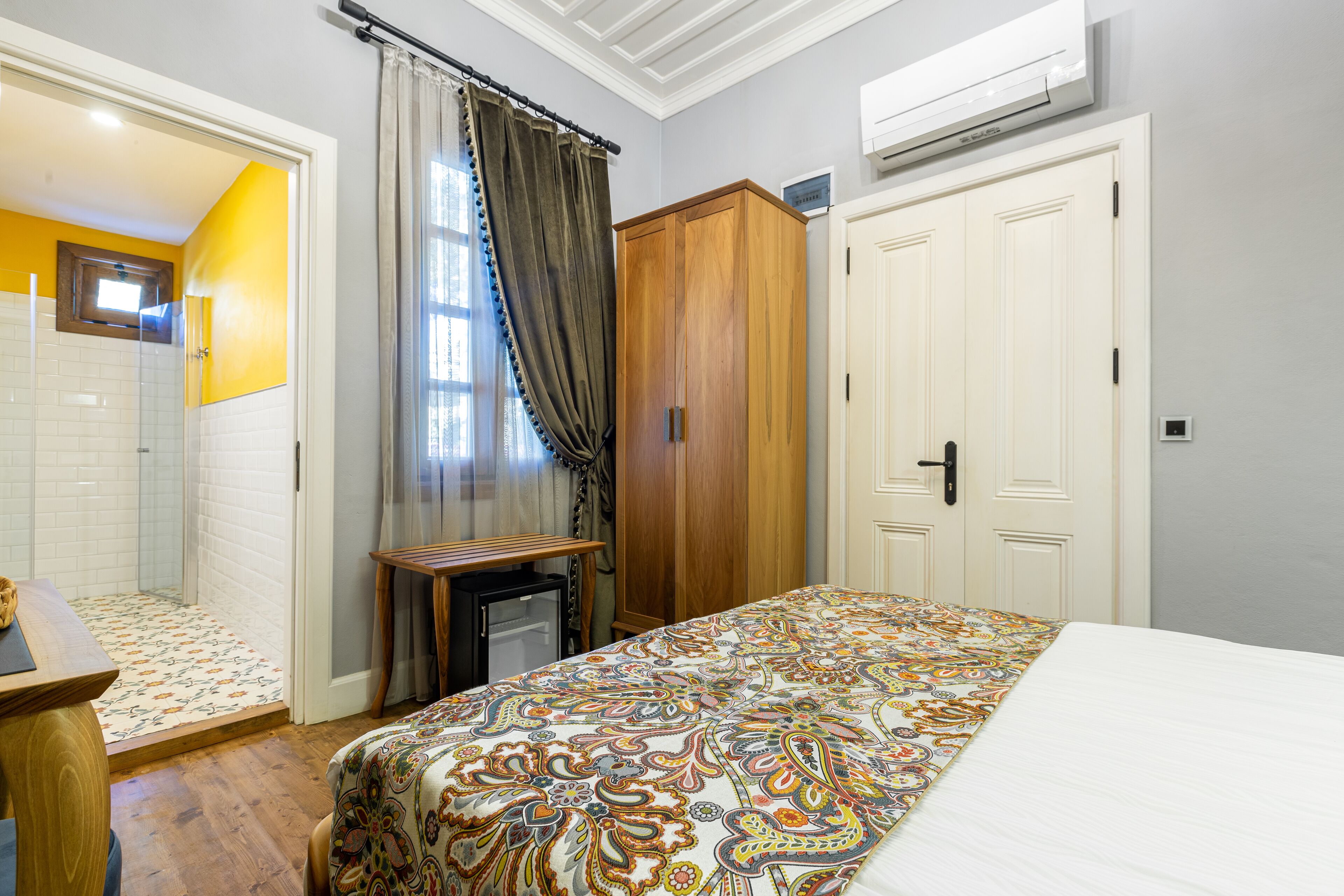 Un dormitorio con una cama, un armario de madera, una mesita pequeña y una zona de ducha con suelo de baldosas.
