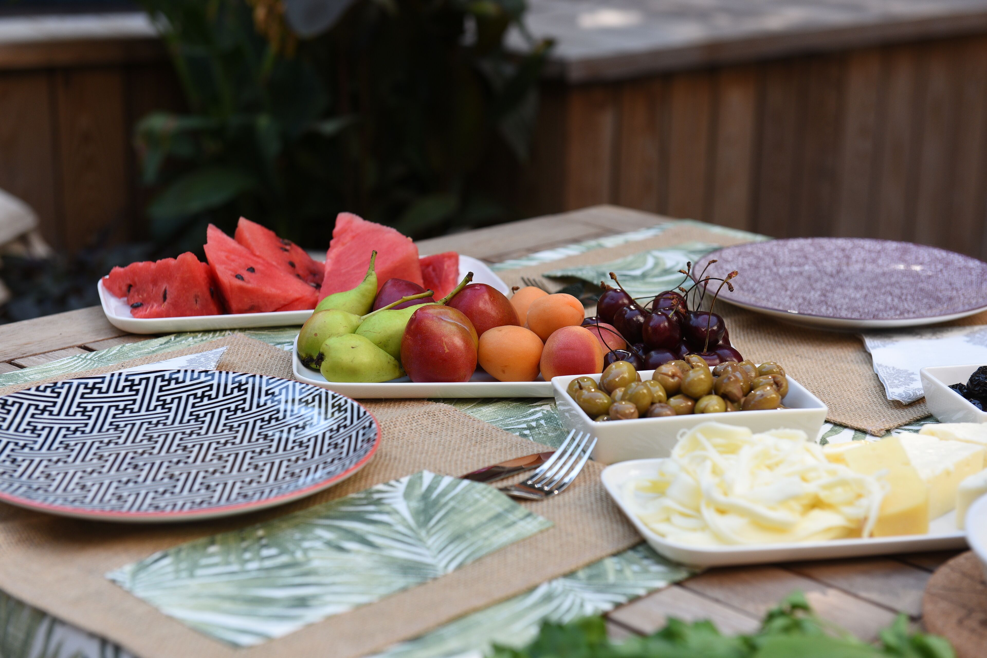 Mesa posta com frutas, queijos e azeitonas diversas, sugerindo uma refeição ao ar livre.