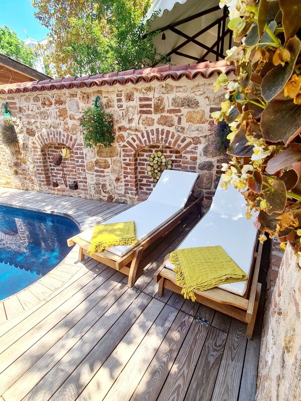 A poolside area with two sun loungers, a stone wall, and a tiled swimming pool. - Hotel Lykia Old Town (Antalya)