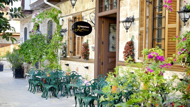 Um café com mesas ao ar livre, um edifício de pedra e uma placa com a inscrição "Lukia".