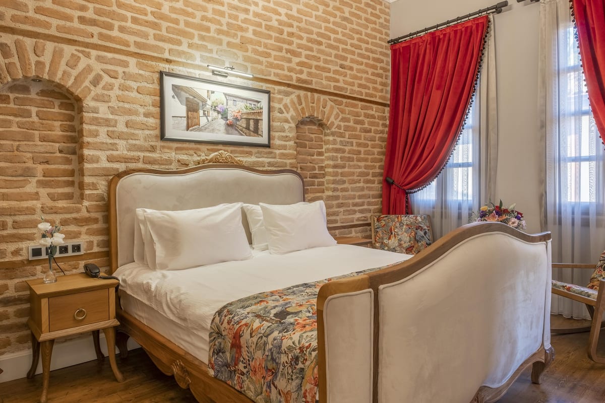 Una camera da letto con parete in mattoni, un letto con biancheria bianca, un comodino e una sedia con cuscino floreale.