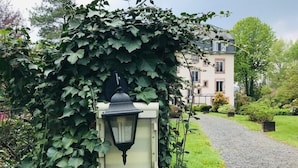 A pathway leading to a building surrounded by lush greenery and a traditional-style lamp post. - Les Jardins d'Aïka (Raon-l'Etape)