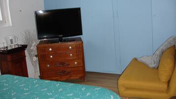 Un dormitorio con una cama, un aparador de madera con televisión de pantalla plana, un sillón amarillo y una ventana con persianas.