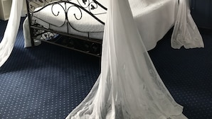 A four-poster bed with a canopy, a bedside table, a lamp, and a wall-mounted shelf. - Les Jardins d'Aïka (Raon-l'Etape)