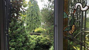A view through a glass door with a decorative swan design, leading to a well-maintained garden with a lawn and various shrubs. - Les Jardins d'Aïka (Raon-l'Etape)