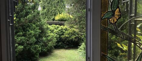 Une vue à travers une porte vitrée ornée d’un motif de cygne décoratif, donnant sur un jardin bien entretenu avec une pelouse et divers arbustes.