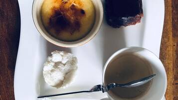 A white plate with a dessert consisting of a caramelized top, a piece of dark chocolate, a scoop of ice cream, and a cup of coffee.
