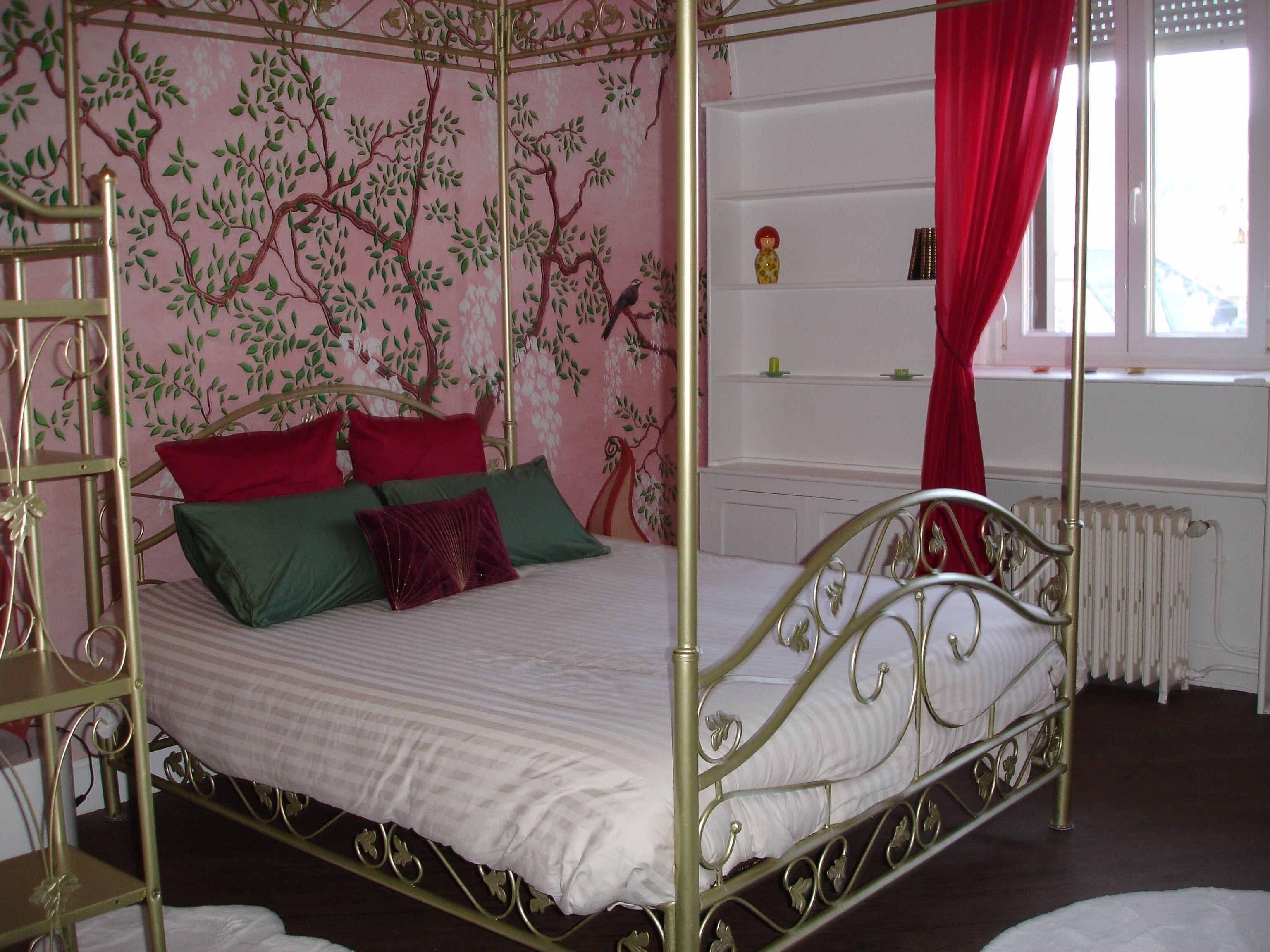 A four-poster bed with a metal frame, green and red pillows, and a white bedspread.