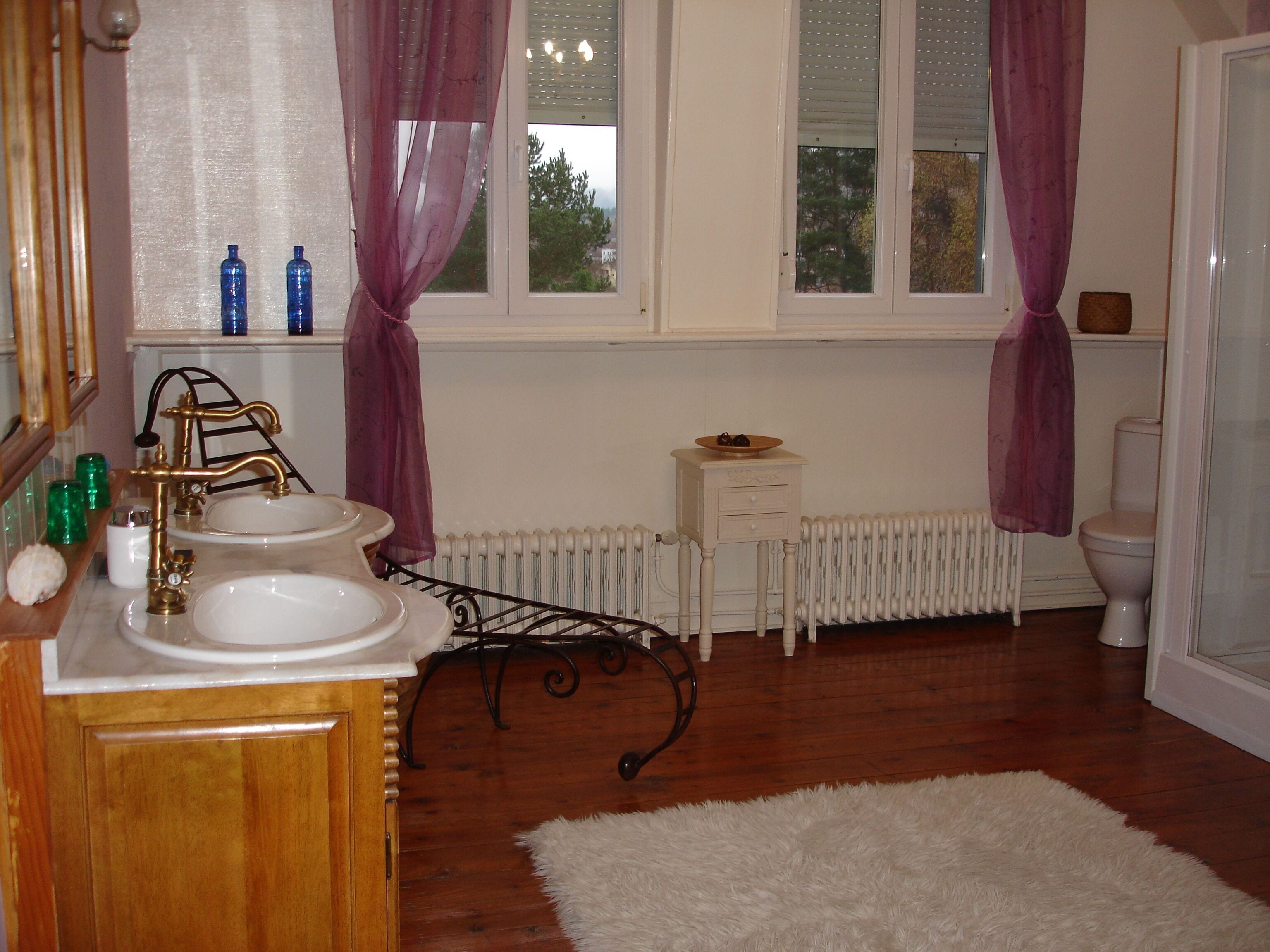 A bathroom with a wooden vanity, a white sink, a mirror, a radiator, and a toilet.