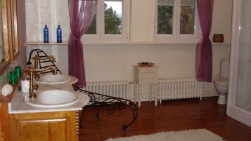 A bathroom with a wooden vanity, a white sink, a mirror, a radiator, and a toilet.