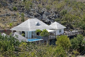 Uma casa com piscina, alpendre coberto e vista para o terreno rochoso.