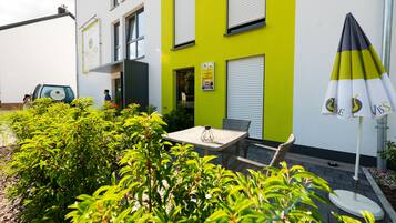 Un edificio moderno con fachada verde brillante, una mesa y una silla afuera, y un cartel que indica ahorros de energía.