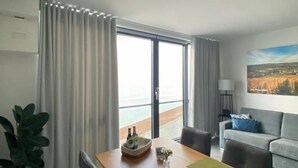 Una sala de estar moderna con una mesa de comedor de madera, un sofá gris y vistas al mar a través de amplios ventanales.