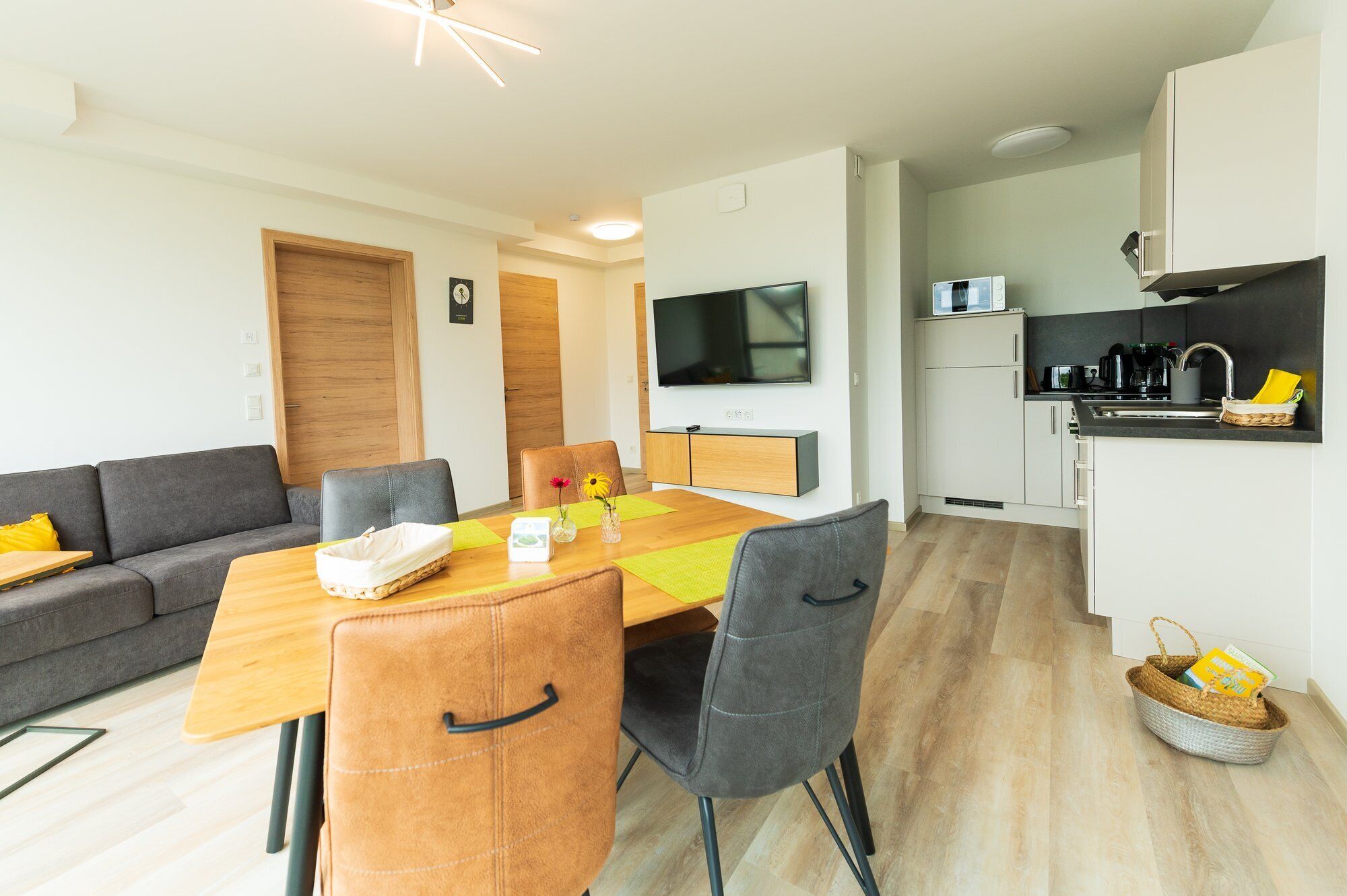 Una sala de estar moderna con un sofá, una mesa de comedor con sillas, un televisor y una zona de cocina con microondas y cafetera.