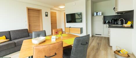 Una sala de estar moderna con un sofá, una mesa de comedor con sillas, un televisor y una zona de cocina con microondas y cafetera.