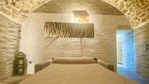 Um quarto com teto de arco de pedra, cama com cabeceira estampada em padrão de zebra, relógio fixado na parede e lareira.