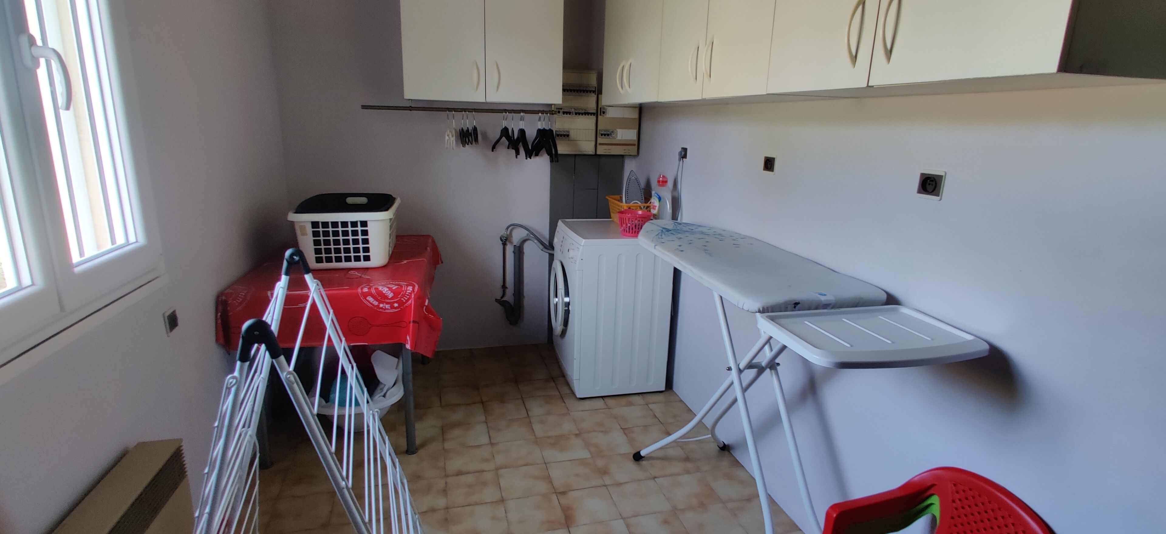 Una sala de lavandería con lavadora, tendedero y una mesa con tela roja.