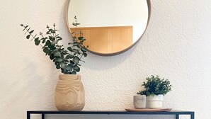 Een zwarte metalen console tafel met een ronde spiegel erboven, een geweven mand en een wit kussen.