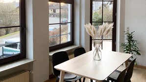 Een eethoek met een tafel, stoelen, grote ramen en een hanglamp.