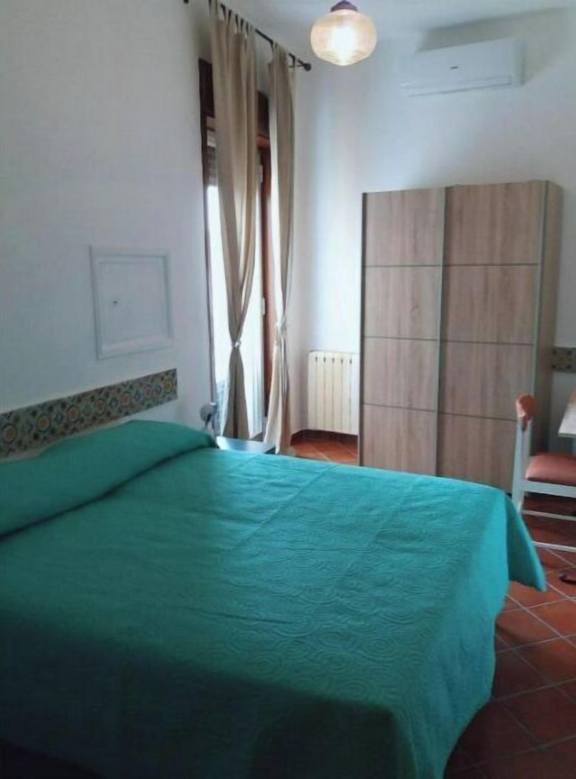 Ein Zimmer mit einem Bett, einem Kleiderschrank, einem Heizkörper und einem fenster mit Vorhängen.