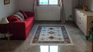 A living room with a red sofa, a patterned rug, a radiator, and a window with curtains. - Miscale House (Cattolica Eraclea)